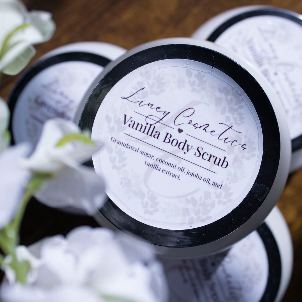 Four body scrubs stacked on top of each other with soft white flowers framing the photo.