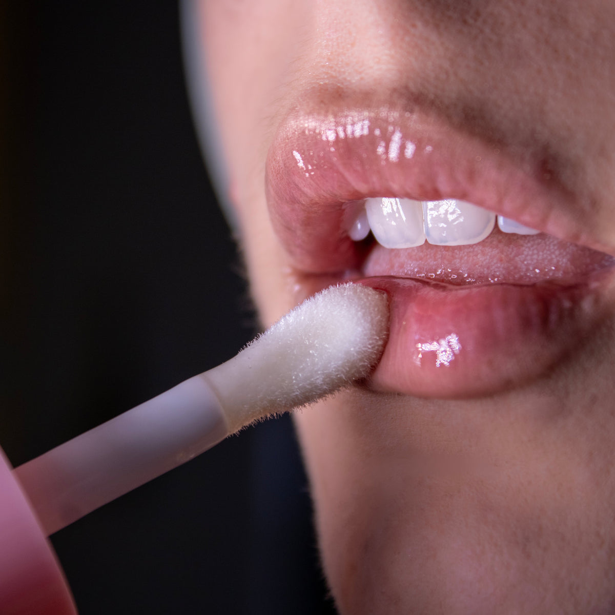 Close-up of a person applying a Healing Lip Oil from a pink applicator wand to their lips.