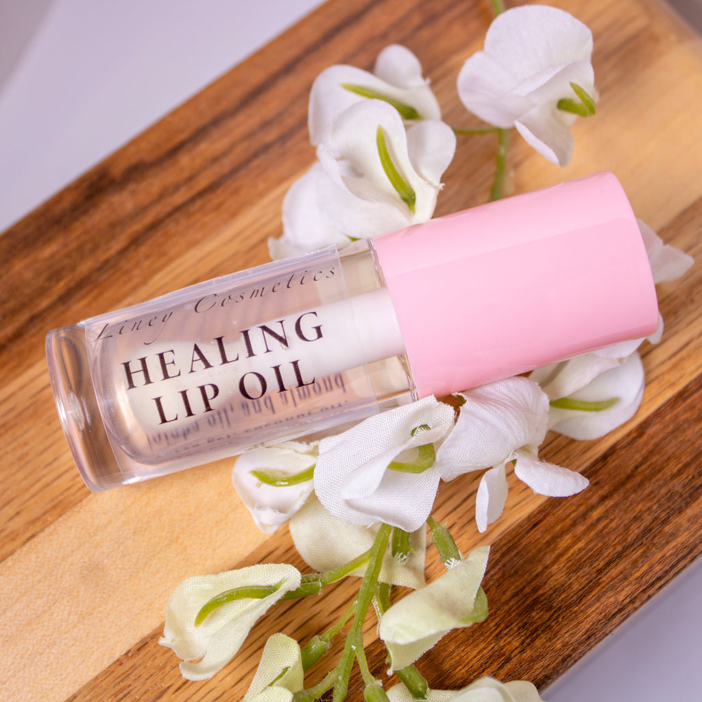 A bottle of Liney Cosmetics Healing Lip Oil with a pink cap lays on a wooden surface.