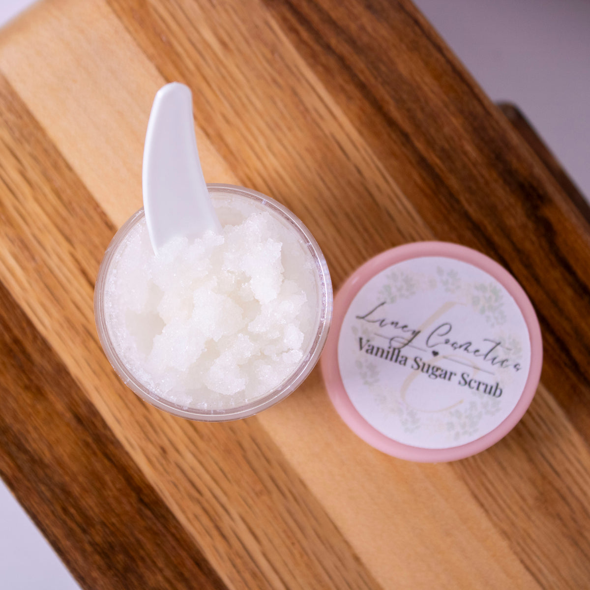 Overhead shot of a small jar of Liney Cosmetics Vanilla Lip Scrub with a white spoon sitting in it.
